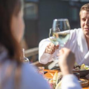 Ein Paar im Bademantel stößt beim Essen in der Sonne mit Wein an.
