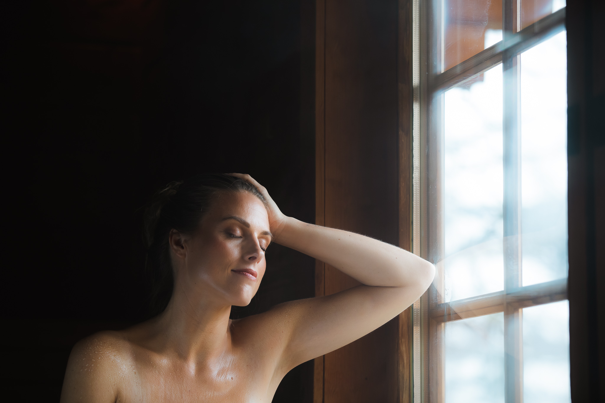 Vrouw geniet met gesloten ogen voor het raam in de Stuga sauna.